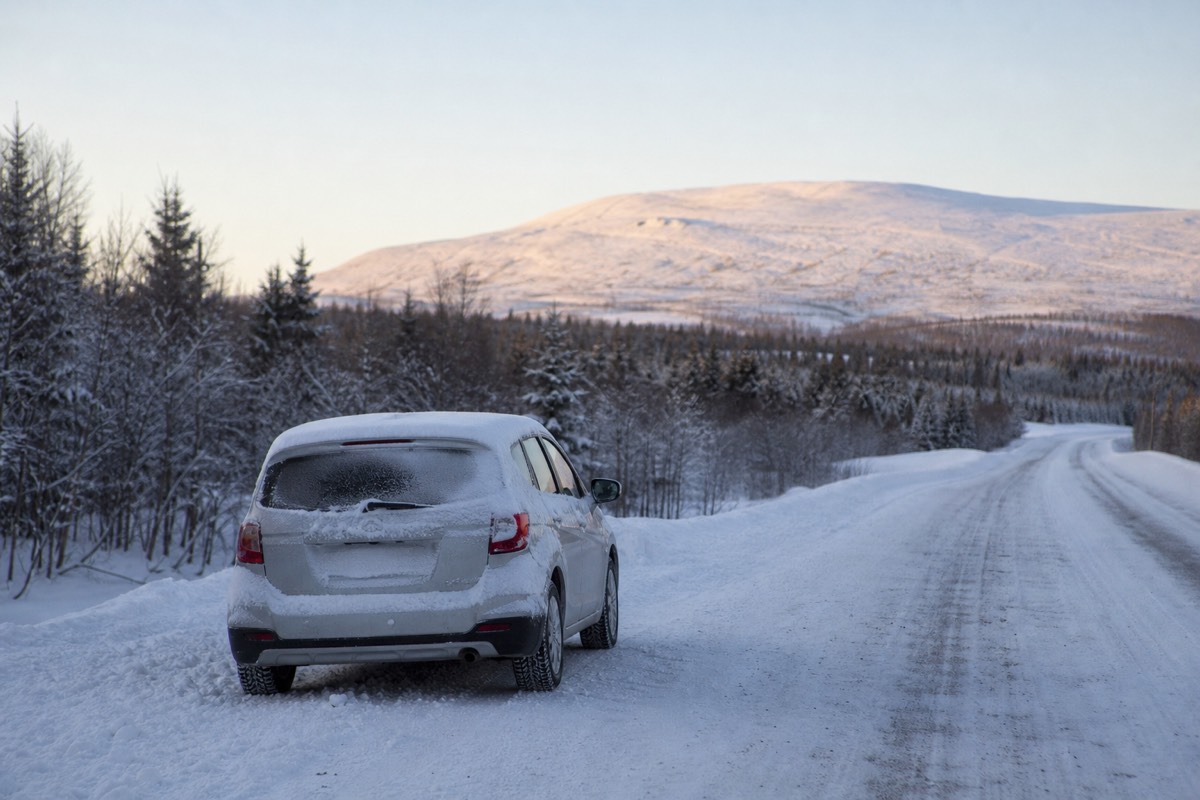 Rental car driving on a snow-covered road in Finnish Lapland at dusk