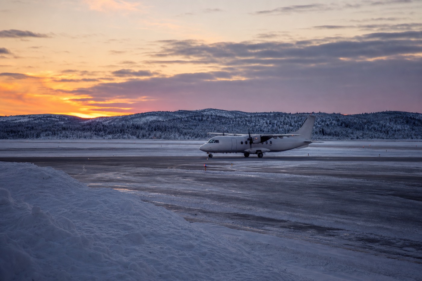 A Finnair aircraft on the tarmac at Rovaniemi Airport with snow-covered pine forest behind it, near the point where the runway crosses the Arctic Circle.