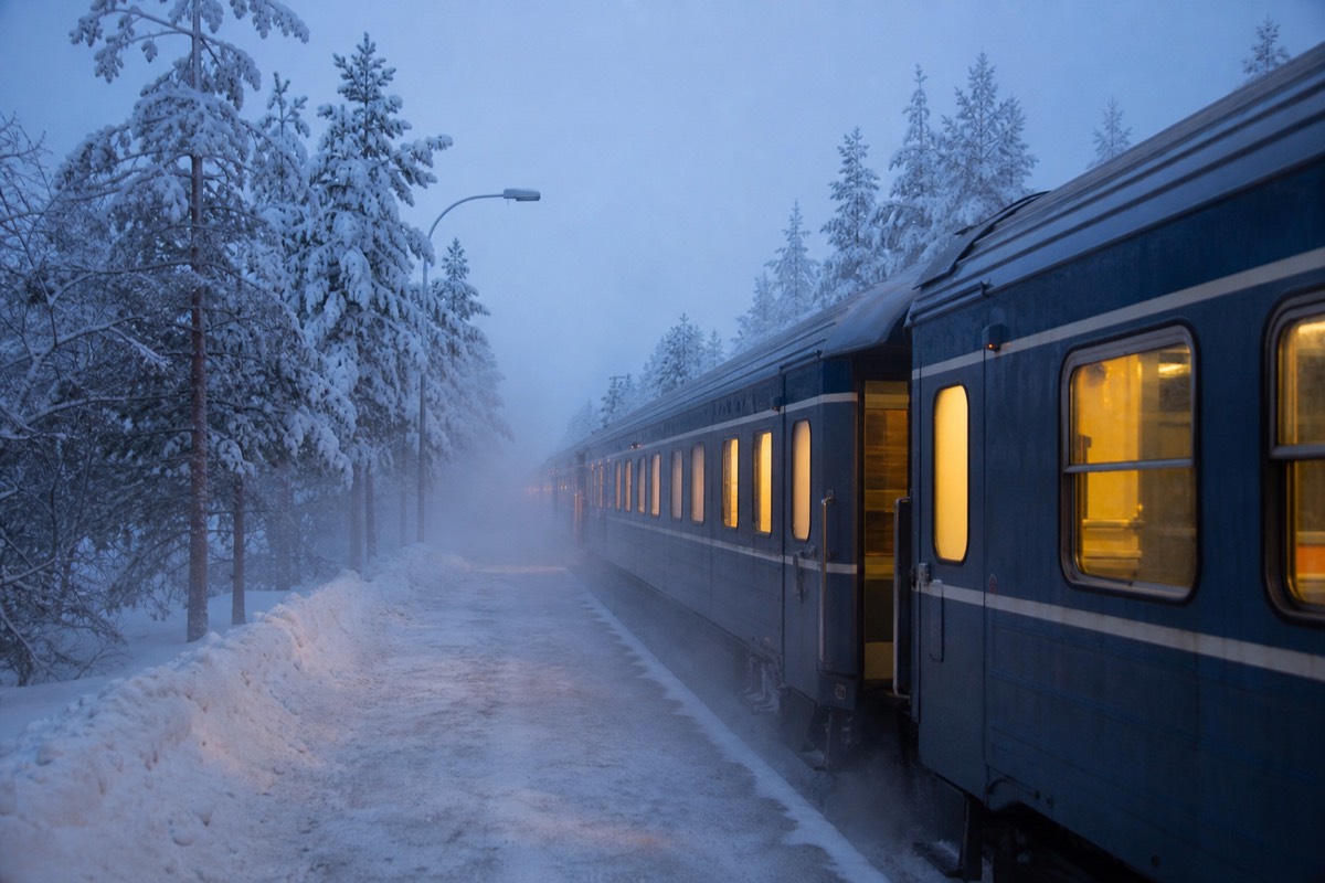 An overnight train arriving through snow-covered Lapland forest