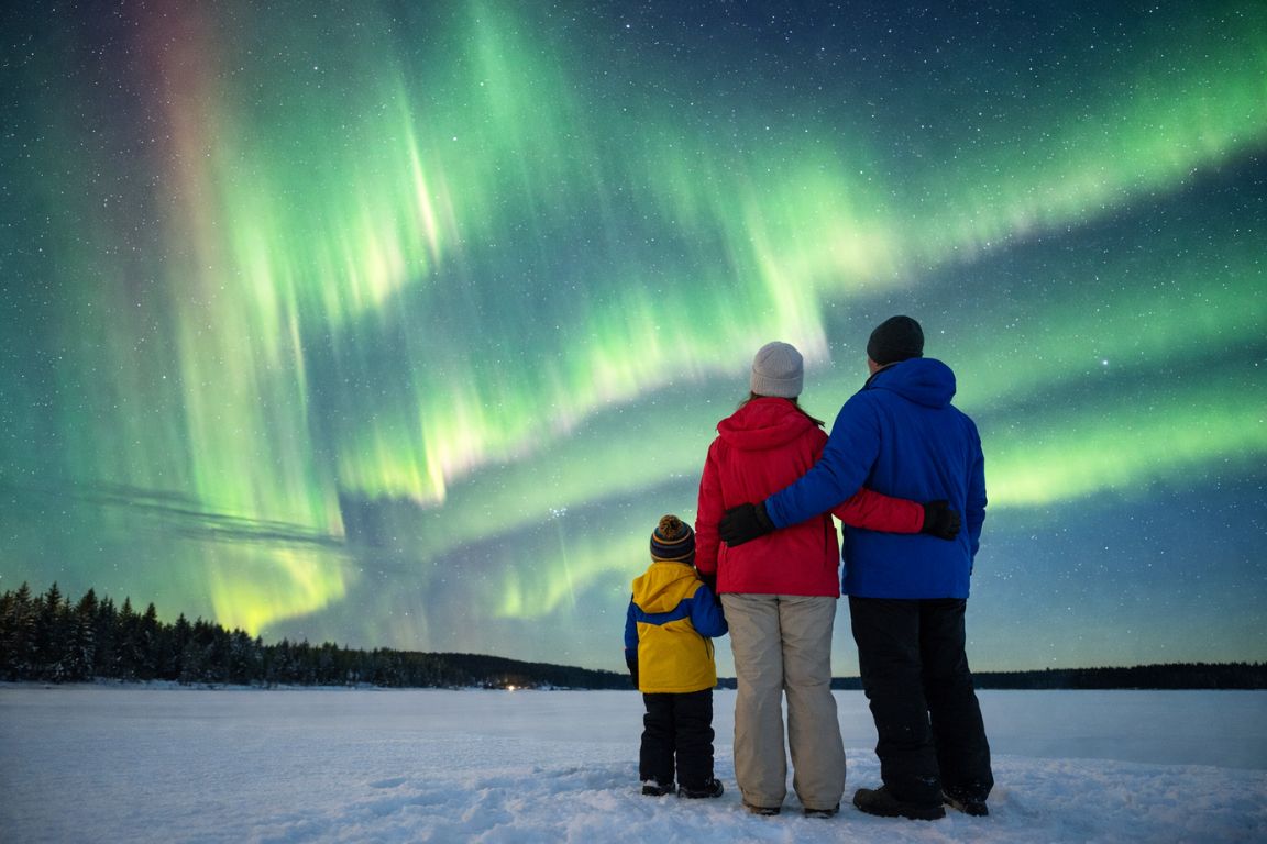 Family watching Northern Lights over snowy landscape in Rovaniemi Lapland under vivid green aurora, captured during a tour with Rovaniemi Tours